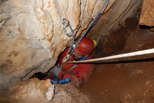 Speleologo visto dall'alto che scende in una grotta illuminata da un fanale